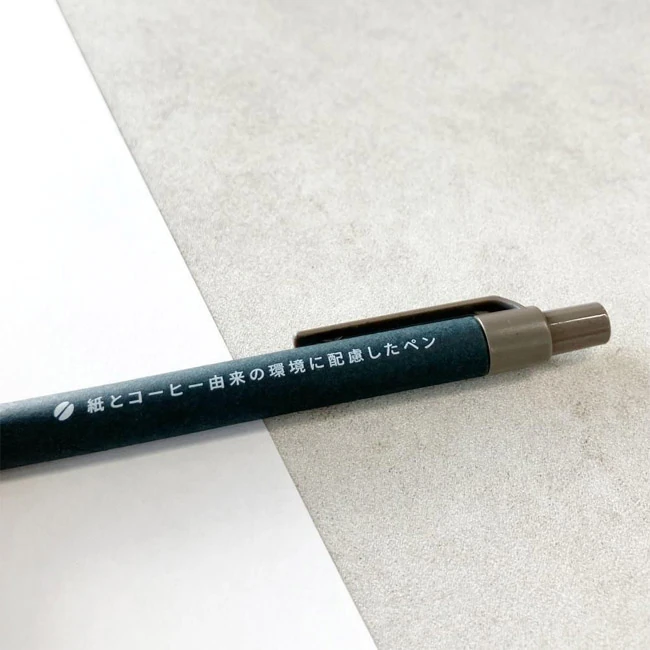 ボールペン【ECO】ノック（HT-7555S）（SNS-0800060）　白い紙の上に斜めに置いたペンのクローズアップ、素材説明の刻印文字が見える